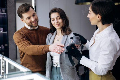 Young couple selecting luxury jewelry, receiving assistance from a professional sales consultant in a modern boutique store