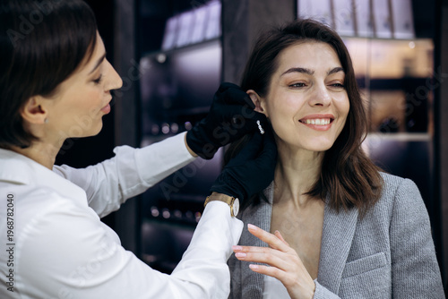 Jewelry consultant helping a smiling woman trying on diamond earrings at a luxury boutique, offering premium service and style