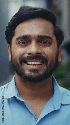 Portrait of handsome Indian man smiles as looks at camera on city street vertical shot. Young entrepreneur with black beard radiates confidence and success in urban block closeup