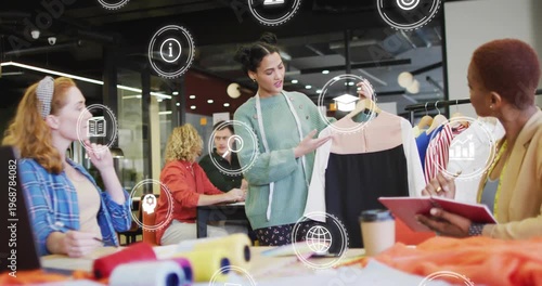 Holding designer in green sweater raising two-tone dress on hanger in studio, with measuring tape