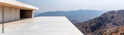 A stark concrete platform extends into a breathtaking panorama of layered, rugged mountains, embodying the serene contrast between minimalist design and nature's vastness. Modern