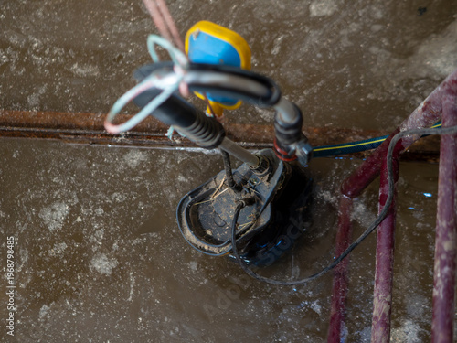 Foto Black electric submersible water pump with yellow float switch operates in muddy brown wastewater to drain flooded residential basement or construction site pit