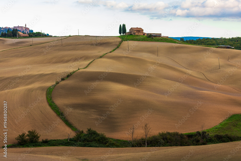 Fototapeta premium Tuscan rolling hills showing agricultural landscape and San Quirico d'Orcia, Italy.
