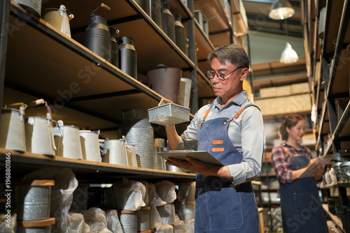 Photography Man in apron checking inventory on shelves filled with metal containers and jars