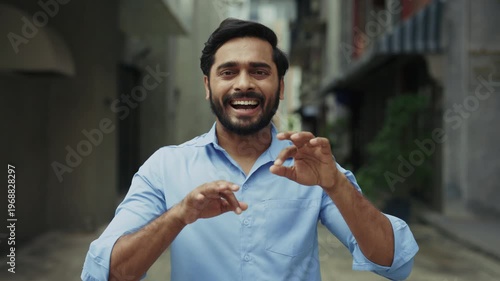 Portrait of friendly Indian man using sign language on city street. Bearded man waving and saying Hi, how are you I'm fine thanks. Communication and inclusion concept.