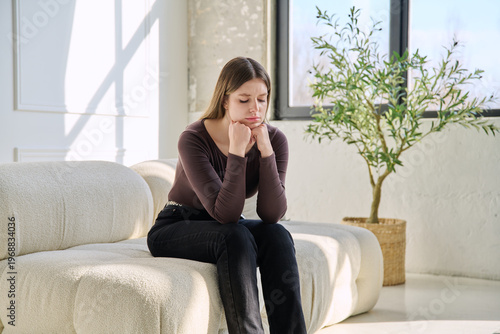 Unhappy upset stressed young woman sitting on sofa at home