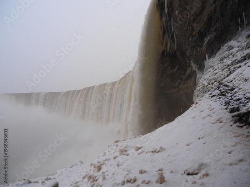 Winter waterfall beside snowy cliff and dark rock wall