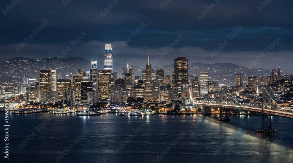 Obraz premium San Francisco skyline, expansive urban skyline after dark, the bay and distant hills layered under maritime haze, illuminated towers rising near the waterfront in cool evening color, featuring