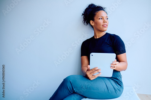 Quadro su tela Young professional woman sitting, holding a modern digital tablet, looking away
