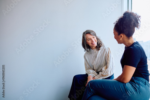 Fotografija Two diverse businesswomen smiling during an informal meeting, engaging in a plea