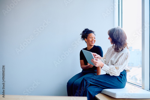 Obraz na plátně Diverse businesswomen discussing work using a tablet while sitting in a modern o