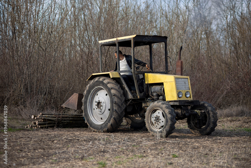 Obraz premium Farmer operating yellow tractor in rural field clearing wood