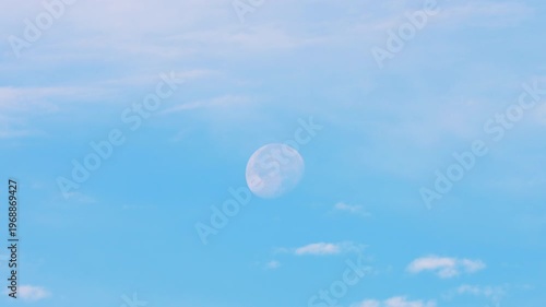 Big moon in the blue sky during the daytime. Feather clouds.