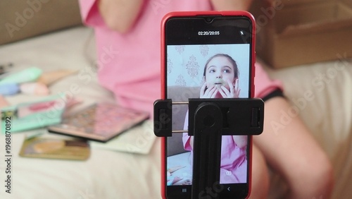 A beauty blogger, a girl dressed in a pink T-shirt, applies eye patches, films videos about her daily skincare routine, and reviews cosmetic products on social media. She films the videos on her phone