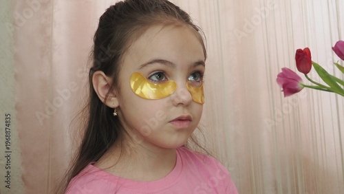 A beauty blogger, a girl dressed in a pink T-shirt, applies eye patches, films videos about her daily skincare routine, and reviews cosmetic products on social media. She films the videos on her phone