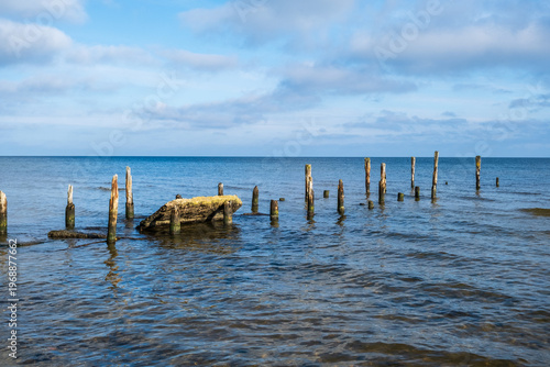 Old wooden pier pilings in the sea under a blue sky.