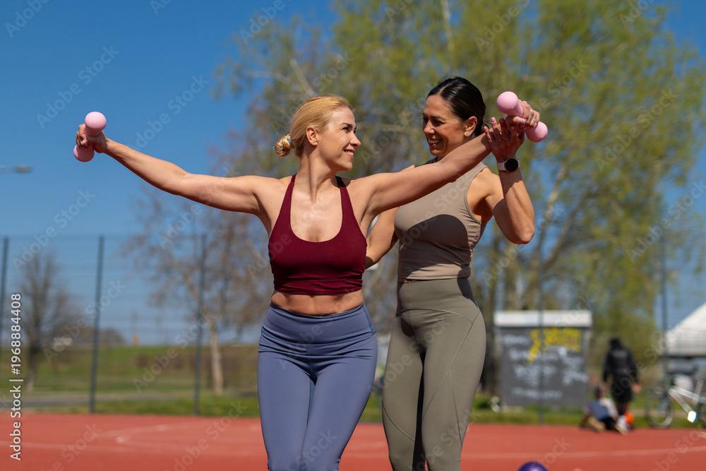 Obraz premium Personal trainer helping woman exercising with dumbbells outdoors