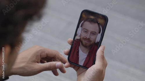 Man hand holds smartphone during video call on city street closeup. Young red haired male freelancer talks to colleague online phone screen view. Business communication technology