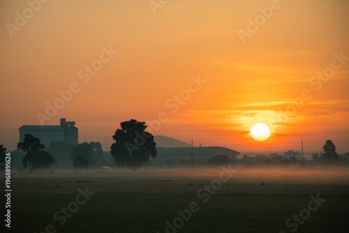 Sunrise over misty countryside with industrial silhouettes — a serene blend of nature and structure