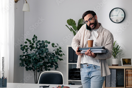 Young man multitasking while talking on phone and carrying work items