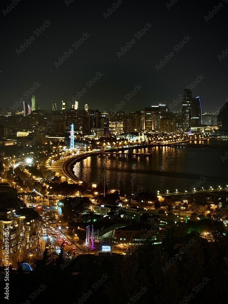 Fototapeta premium Night waterfront skyline with curving boulevard lights, conveying urban glamour, travel romance, city energy, and evening tourism atmosphere.
