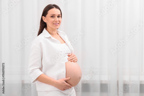 Beautiful pregnant woman touching her belly near curtains at home, space for text Free Download Beautiful pregnant woman touching her belly near curtains at home, space for text - GFXLoad