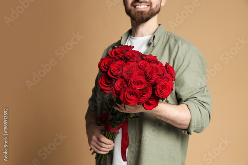 Man with bouquet of roses on beige background, closeup