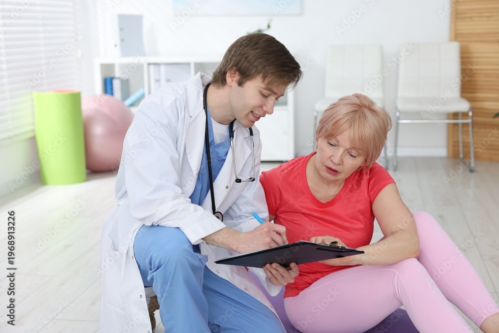 Fototapeta premium Senior woman and physiotherapist with clipboard indoors