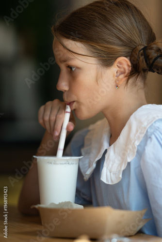 Teenage girl drinking refreshing milk drink through a straw in a cafe, close-up.