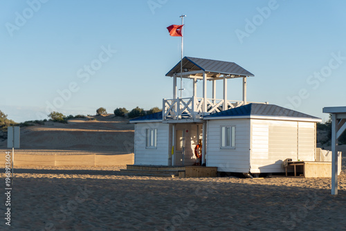 A lifeguard tower with a red flag on its spire on the beach early in the morning.