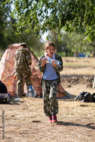 A girl in a tent city carries a bottle of water in her hands