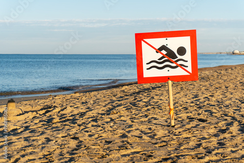 No swimming sign on the beach near the sea. In the background blue sea and sand.
