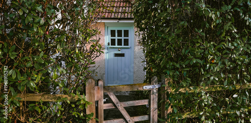 Foto Quaint cottage door appearing behind a rustic wooden gate and lush green hedge,