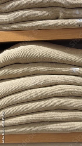 A neat stack of new sweaters in light and blue colors with visible size stickers, presented on a store shelf. This clip is perfect for showcasing seasonal apparel collections, retail organization, and