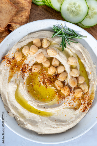 Hummus on a wood cutting board with cucumbers, peppers, pita chips and olive oil 