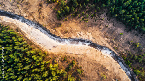 Dried riverbed snaking through a green forest and barren land, environmental change from above