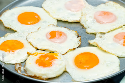 Repetitive pattern of fried eggs with fully cooked yolks on metal tray, culinary texture background