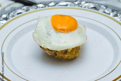 Close-up of Ecuadorian bolón mixto with fried egg on white plate, traditional Latin breakfast dish