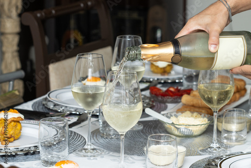Close-up of hand serving sparkling wine into glasses at elegant table setting, festive gathering