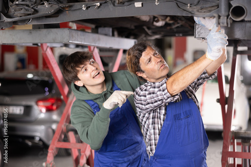 Young auto mechanic helps an experienced auto mechanic repair a car in a car service center