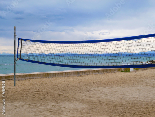 Fotografía Beach volleyball net on empty seaside court with dramatic cloudy sky and ocean v