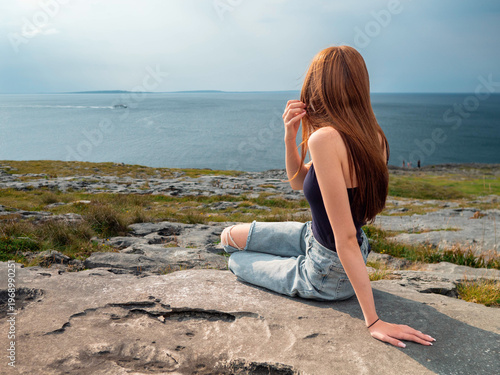 Εκτύπωση καμβά Woman sits on rocky cliff, gazing out at ocean