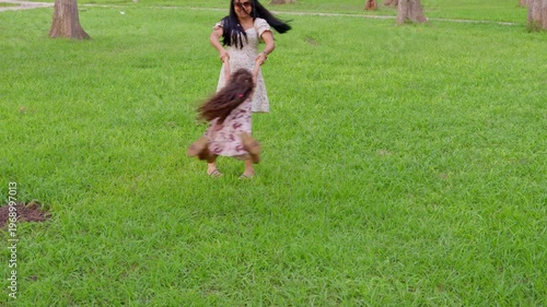 Playful mother spinning her daughter around in a green park