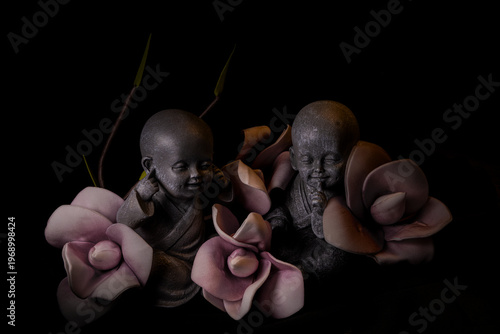 Two miniature monk statues with flowers on dark background zen meditation and spirituality concept