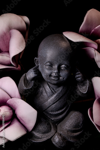 Zen monk statue covering ears with flowers close up mindfulness and meditation concept