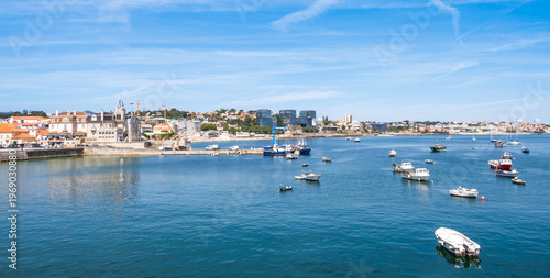 Cascais harbor with traditional fishing boats and modern cityscape, Portugal. Panorama of Atlantic ocean waters and modern glass buildings contrasting with historic palace architecture in old town