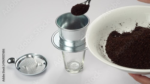Woman scoops ground coffee into a traditional Vietnamese phin filter. High-key bright commercial footage of authentic Asian coffee preparation.