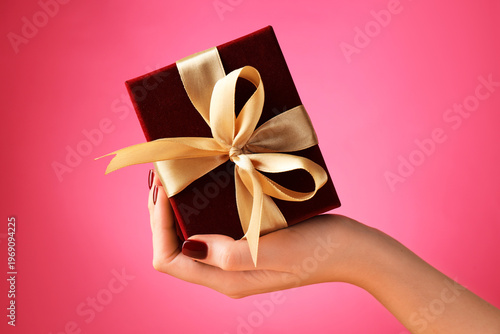 Woman holding elegant gift box with bow against pink background, closeup