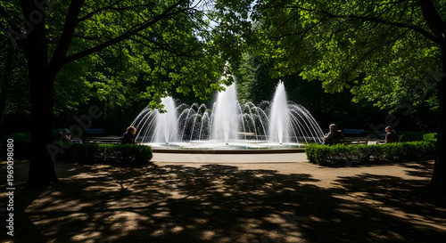 Fountain in Park with Lush Greenery and Sunlight Filtering Through Trees