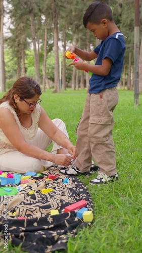 Mother tying son's shoes while he plays with building blocks at the park